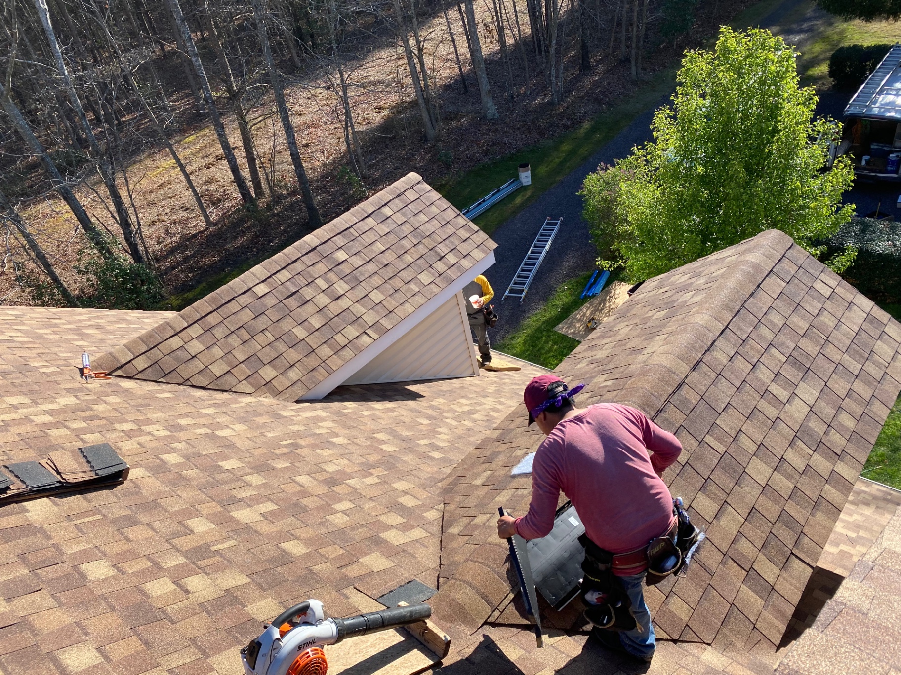Aerial view of the crew installing architectural shingles on a wooded property