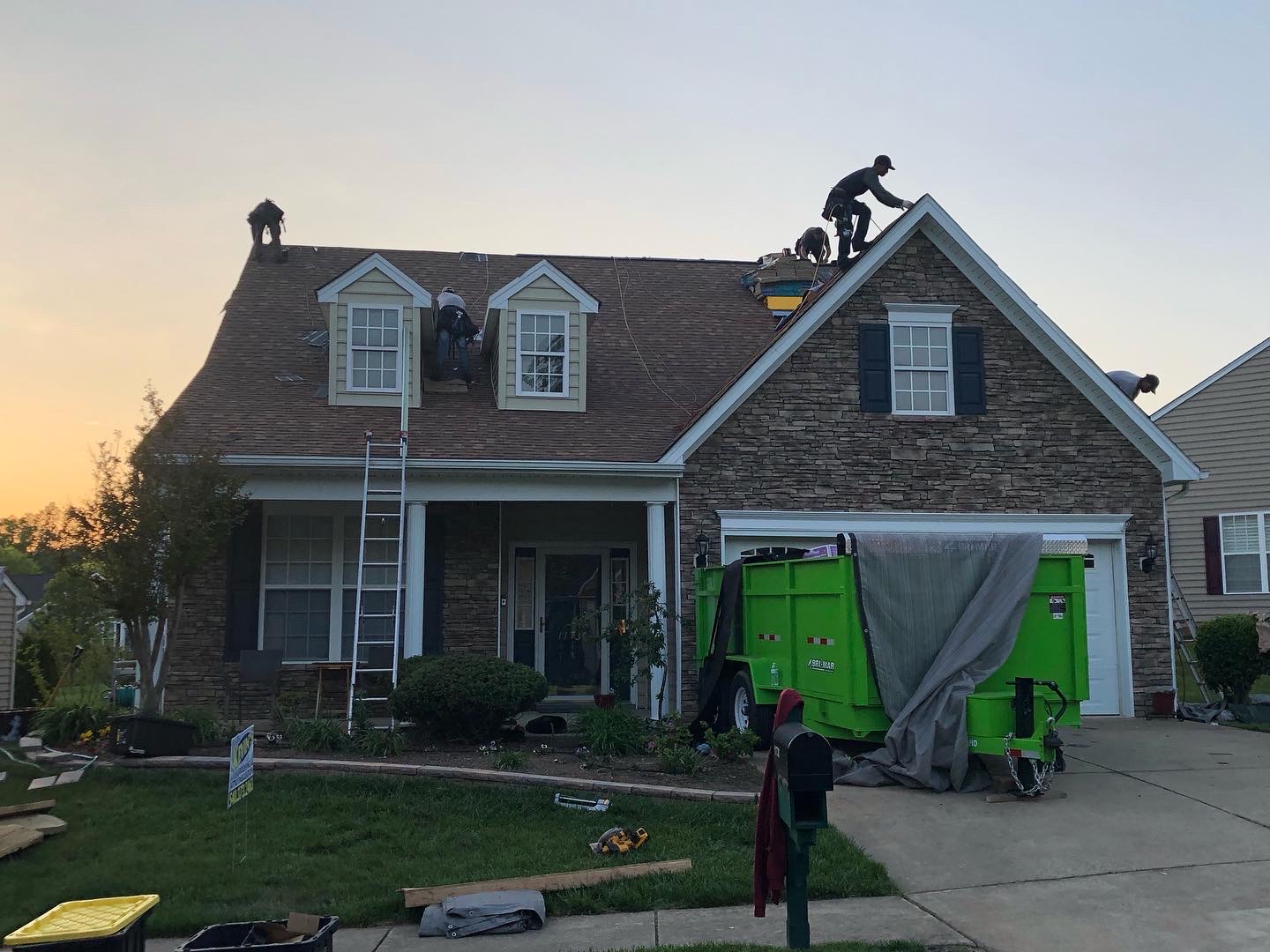 Magic RoofWorks crew installing a new roof at sunset on a stone-front home