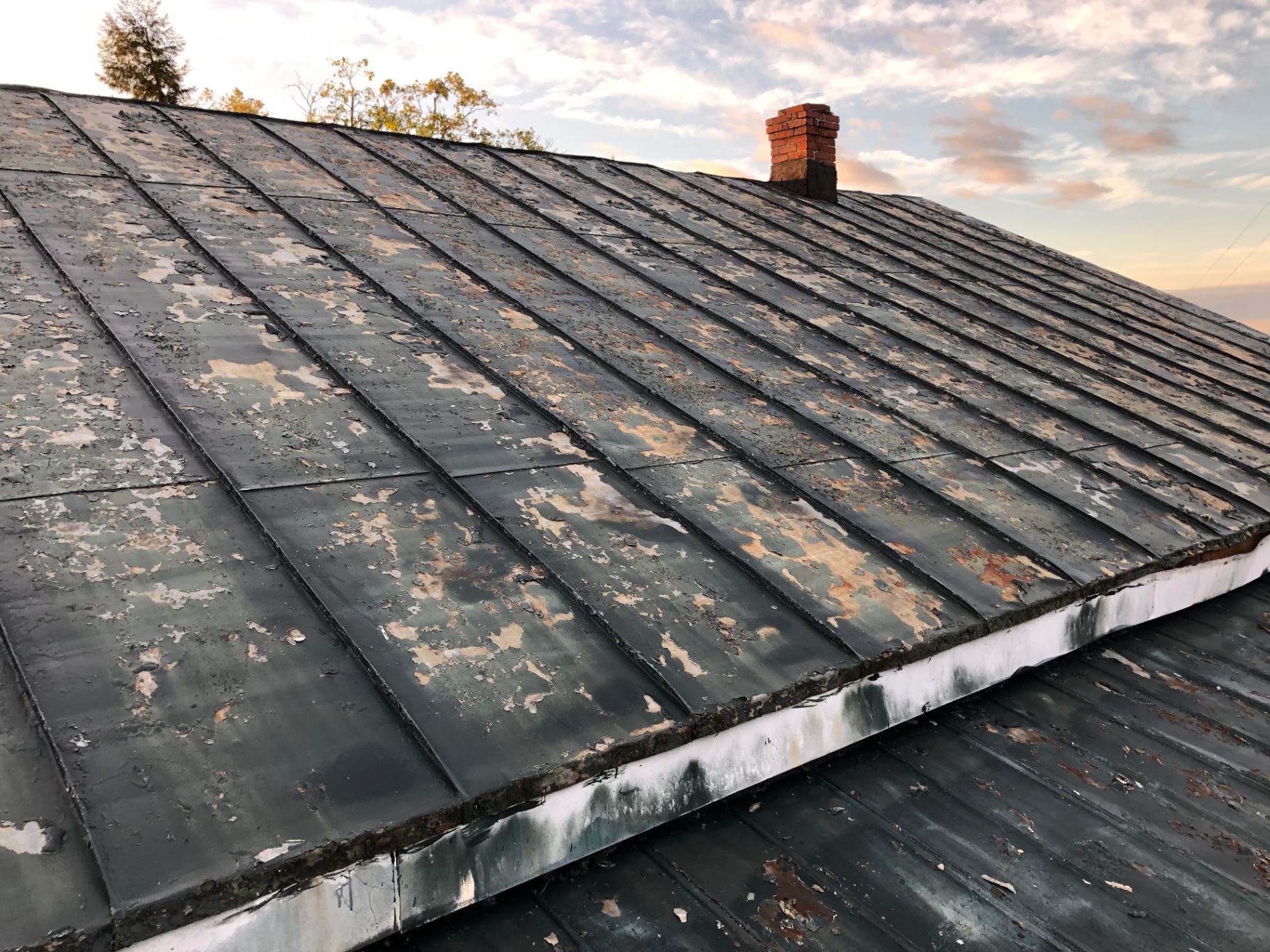 Failing painted metal roof with peeling coating before replacement