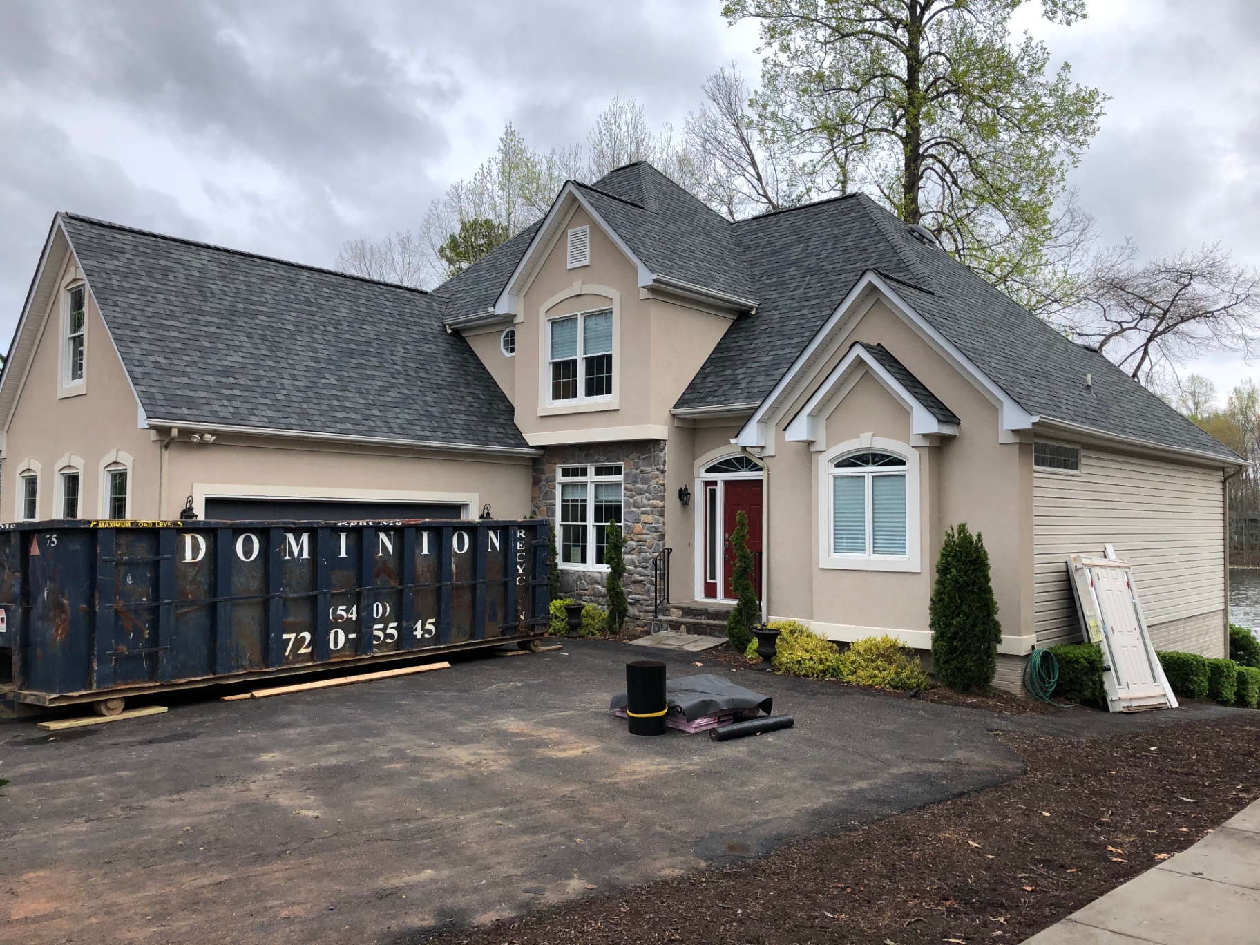Stucco lake home during a full roof replacement with dumpster on site